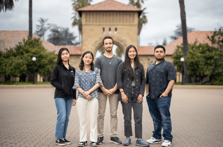 Five people stand in a row before an arch in Main Quad.